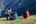 a group of people sitting on a hill with mountains in the background