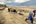 two people walking on a dirt path with donkeys
