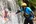 a man and woman in helmets holding each other in front of a waterfall