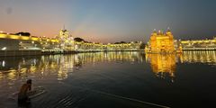 a body of water with buildings and lights with Harmandir Sahib in the background