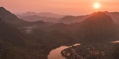 a river running through a valley with mountains and a city in the distance