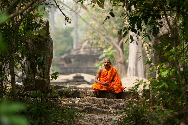 a monk sitting on a stone path in the woods