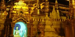 a large gold building with a statue in the background with Shwedagon Pagoda in the background