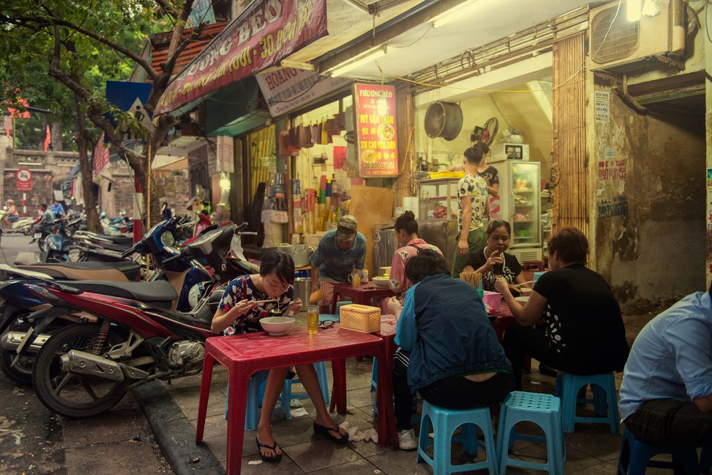 Women sitting and eating a steaming bowl of pho in Hanoi