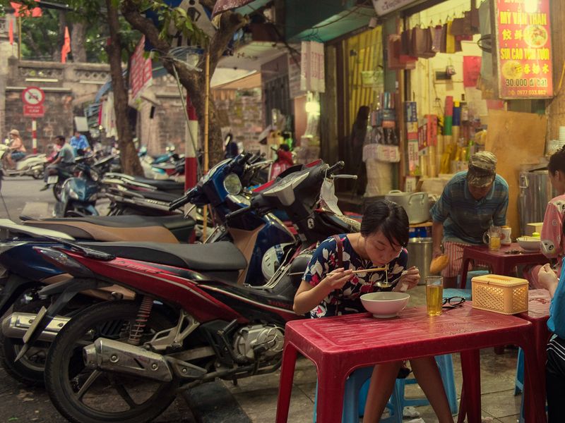 Women sitting and eating a steaming bowl of pho in Hanoi